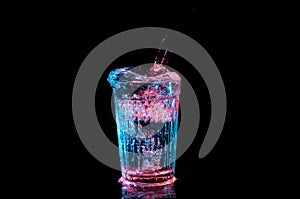 Clear beverage being poured into a vintage glass under red and blue lights isolated on a black background