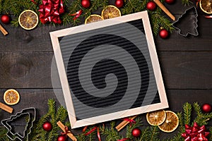 Clear black felt letter board flatlay on dark rustic wood table with Christmas decoration and fir tree boarder. Top view with