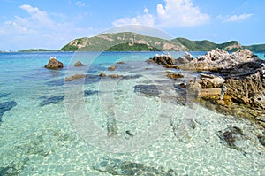 Clear blue sea water with stone and big mountain.