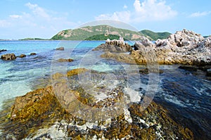 Clear blue sea water with stone and big mountain.