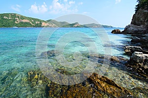 Clear blue sea water with stone and big mountain.