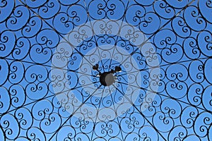 Clear blue sky through black iron wrought scrolled canopy