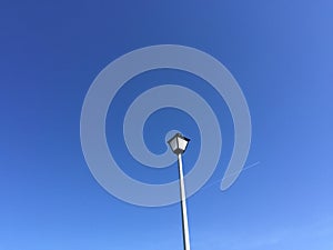 Clear blue sky with lightpost and passing plane