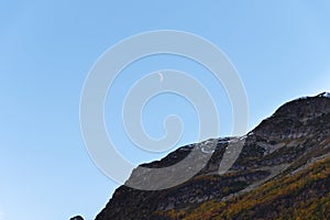 Clear daytime blue sky, mountains and waning white moon