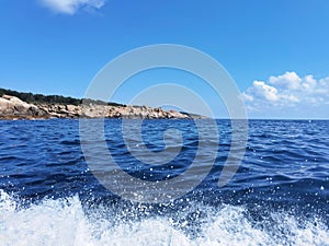 Clear deep blue sea water with white waves and rocks on the horizon. Vacation destination landscape, sunny summer day background