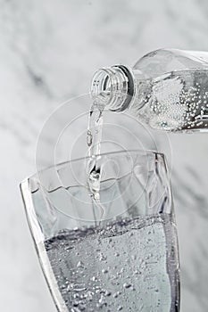 Clear drinking carbonated water is poured into glass on light background. Plastic bottle, splash, beverages, macro, close up,