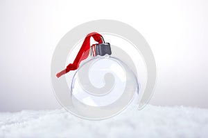 Clear empty Christmas ornament with red ribbon sitting in snow