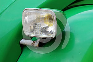 Clear front headlight of old light green vintage car mounted on rusted metal pipe