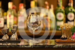 Clear glass on black marble table top and beautiful bokeh shelves with alcohol bottles