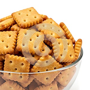 A clear glass bowl filled with golden brown square crackers on a white background biscuits