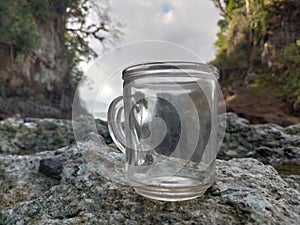 Clear glass cup on the rock on the beach is very pretty with a view of the hill alongside the beach