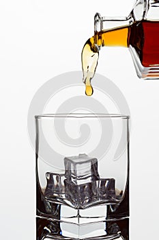 Clear glass glass with ice cubes. Frozen stream from a bottle of whiskey or cognac or brandy on a white isolated background