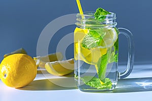 Clear glass mug filled with water, sliced â€‹â€‹lemon and mint leaves with yellow straw,lit up in the morning light.