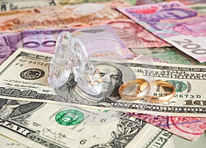 Clear glass pair of shoes and wedding rings on different currencies. Money for love