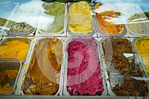 Clear glass showcase showing variety of delicious colorful ice cream flavors, blueberry, coffee, chocolate, vanilla, etc.