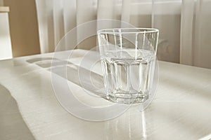 Clear glass of clear water on minimalist table with window light and shadow