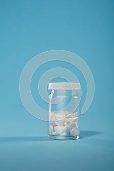 Clear Glossy Plastic Bottle with White Cap and white capsules on blue background