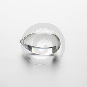 A clear liquid drop sits on a smooth white surface casting a soft shadow