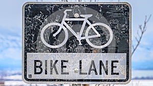 Clear Panorama Bike Lane sign post in front of a tree and snow covered landscape in winter