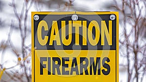 Clear Panorama Close up of a yellow sign that reads Caution Firearms In Use Keep Out