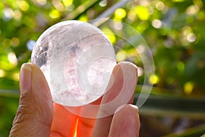 Clear quartz crystal sphere ball with rainbow colour inside it in hand on nature background.