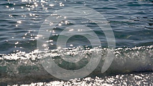 Clear rather calm sea with small waves, sun reflects in water, some seaweed visible, closeup detail from the beach near