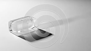 A clear rectangular ice cube rests on a smooth white surface