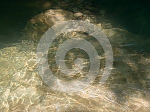The clear river calm water with bright highlights and a rocky bottom is illuminated by the sun's rays. Fullscreen photo
