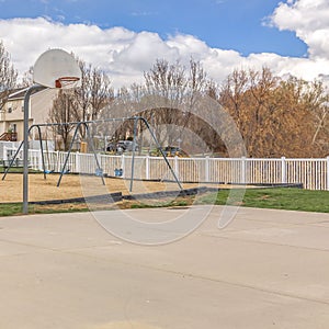 Clear Square Playground and basketball court against homes and blue sky with puffy clouds