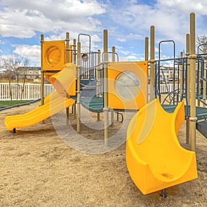 Clear Square Playground with a bright yellow slide under the vivid sky with puffy clouds