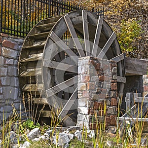 Clear Square Wooden water wheel and flume at a grassy pond viewed on a sunny day