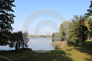 Clear sunny day and calm surface of Lake Birini with deciduous trees on the green shore