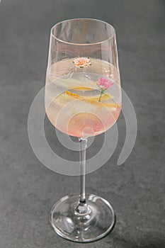 A clear sweet pink sparkling beverage decorated with fruit peels and small roses in a champagne glass.
