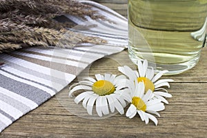 Clear transparent cup of camomile tea on vintage wooden background with dried herbs and daisy flowers.