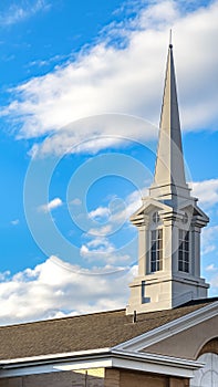 Clear Vertical Exterior of a beautiful church with a white steeple against cloudy blue sky