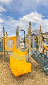 Clear Vertical Playground with a bright yellow slide under the vivid sky with puffy clouds