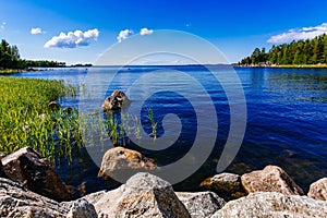 Clear water blue lake with stones and green forest on a sunny summer day in Finland.
