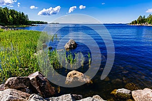 Clear water blue lake with stones and green forest on a sunny summer day in Finland.