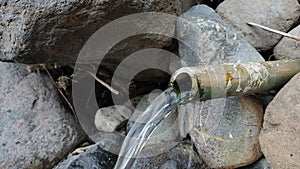 Clear water flows from a bamboo pipe among the rocks