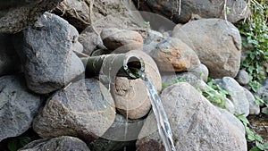 Clear water flows from a bamboo pipe among the rocks