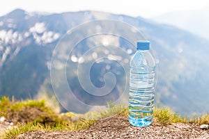 Clear water in a plastic bottle stands on a stone high in the mountains on a sunny day
