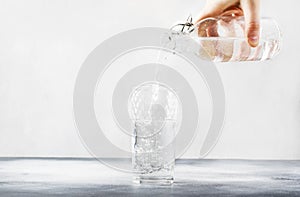 Clear water is poured from glass bottle into glass, gray background, selective focus