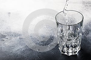 Clear water is poured from glass bottle into glass, gray background, selective focus