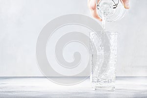 Clear water is poured from glass bottle into glass, gray background, selective focus