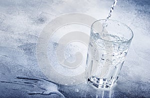 Clear water is poured from glass bottle into glass, gray background, selective focus