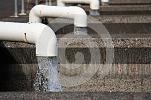 Clear water pours out with force from white curved pipes into concrete basins