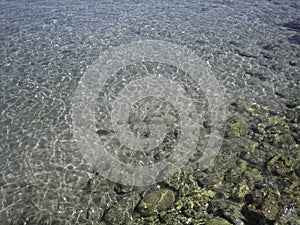 Through the clear water in the rays of the reflection of the sun, you can see the shallow sea floor of sand, pebbles and stones of