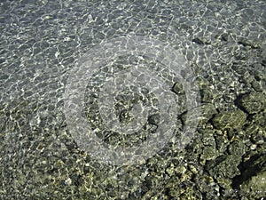 Through the clear water in the rays of the reflection of the sun, you can see the shallow sea floor of sand, pebbles and stones of