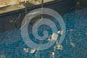 clear water of swimming pool. blue colored bottom of the pool is visible. ladde of stainless steel seen in one side of the pool