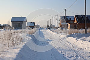 Cleared wide road winter drive  private houses in the Siberian village among the snowdrifts through the forest on a clear winter